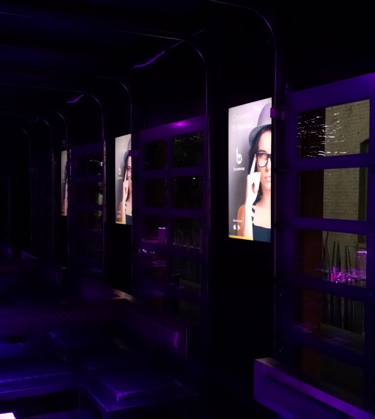 Boomvox ads mounted in booths at a real venue, glowing purple under the club lighting